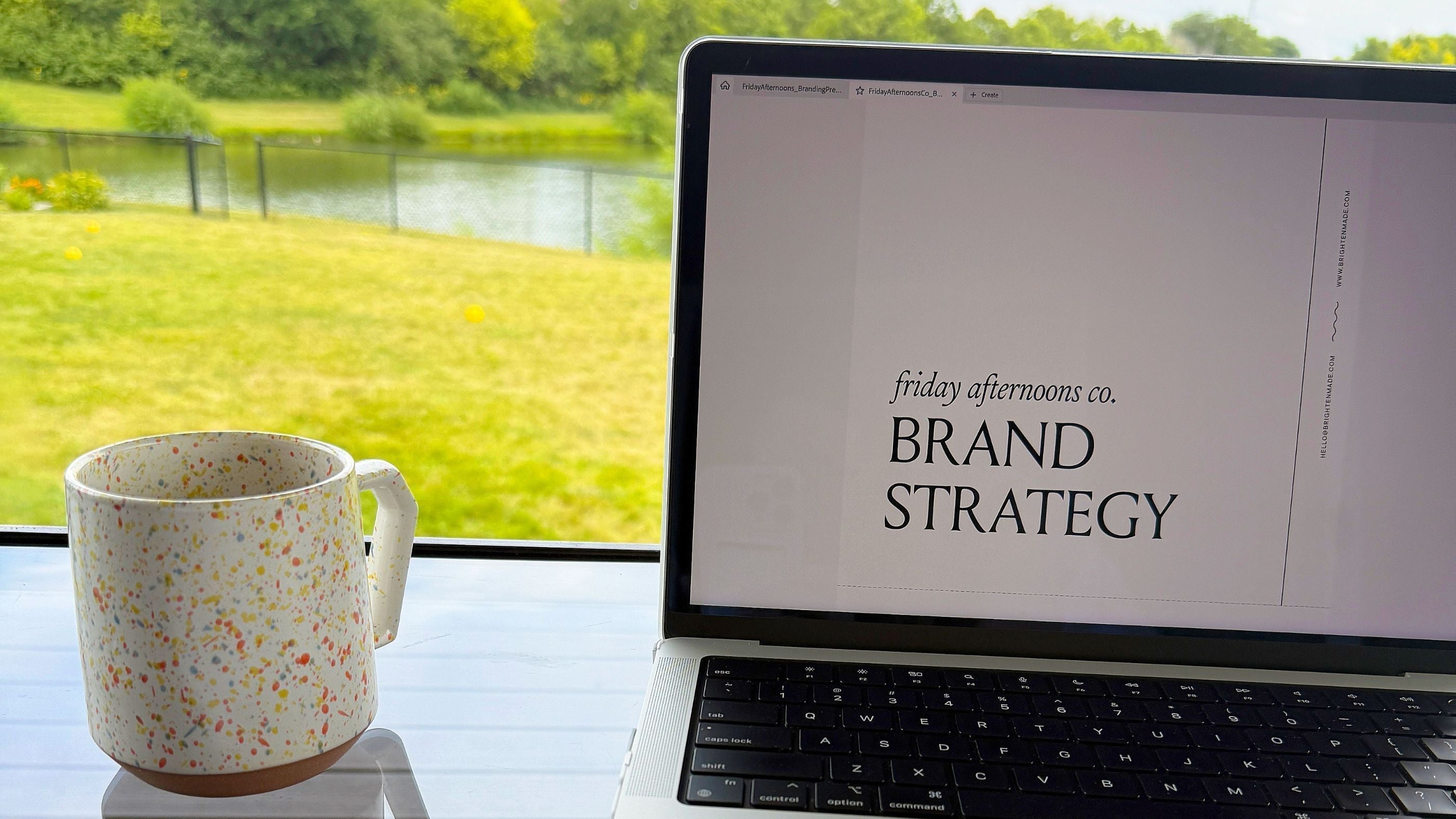 Workspace with laptop showing Friday Afternoons Co. brand strategy, sketchbook with abstract planner design sketches, and speckled coffee mug — view of green yard outside window — representing small business rebrand and creative process for planner brand.