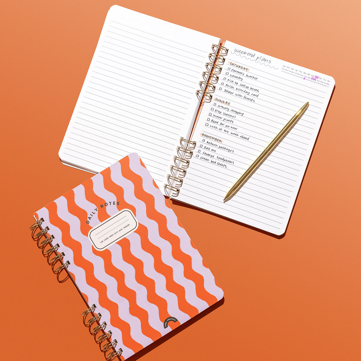 Poppy & Lavender Swirls Daily Notes notebook beside an open lined notebook with handwritten weekend plans and a gold pen on an orange background.