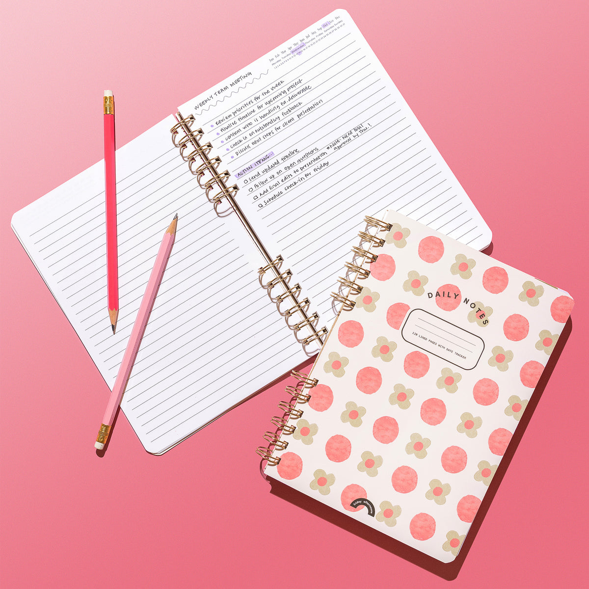 Sage Petals Daily Notes notebook beside open lined pages with handwritten meeting notes and pink pencils on a pink background.