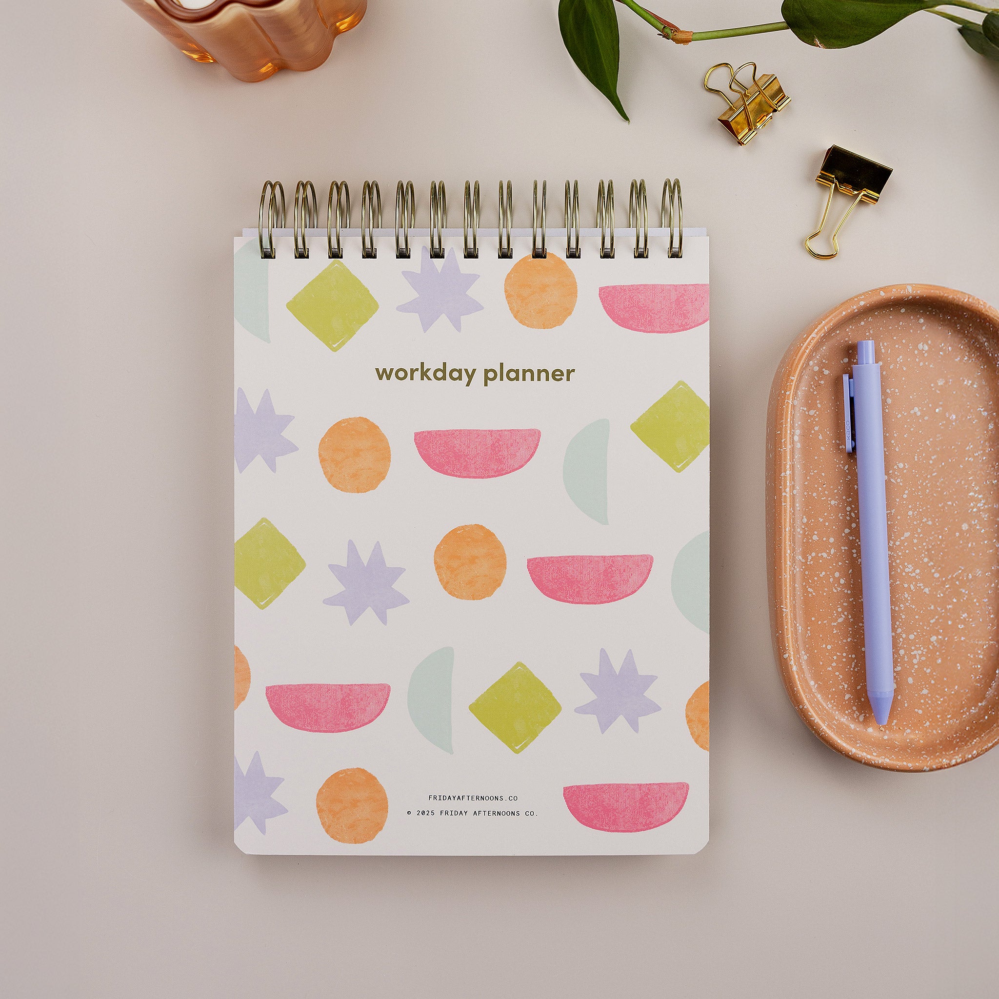 Bright Shapes Workday Planner — top-spiral daily planner for work with pink and green patterned cover on desk.