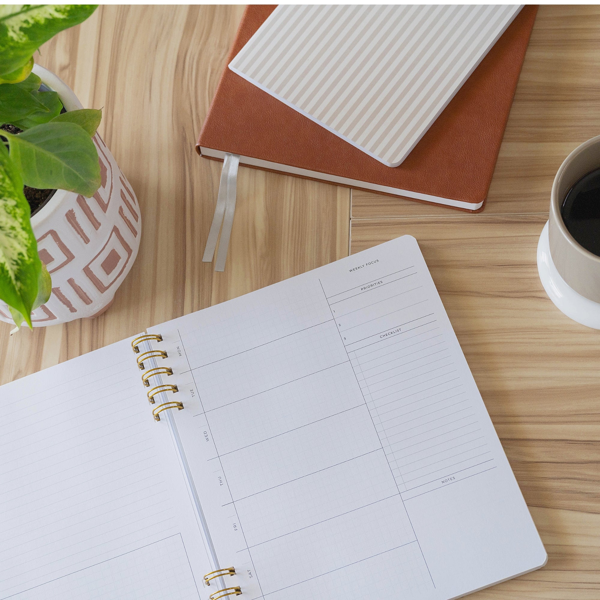 Open quarterly planner on a wooden table with a notebook, plant, and cup of coffee.
