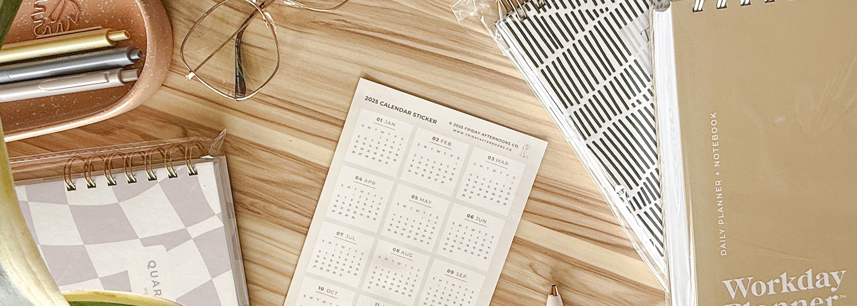 2025 calendar sticker on desk with accessories and an assortment of daily planners