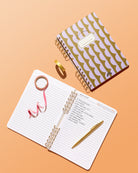 Forest and Lavender Half Moons notebook beside open lined pages with handwritten notes and a gold pen.