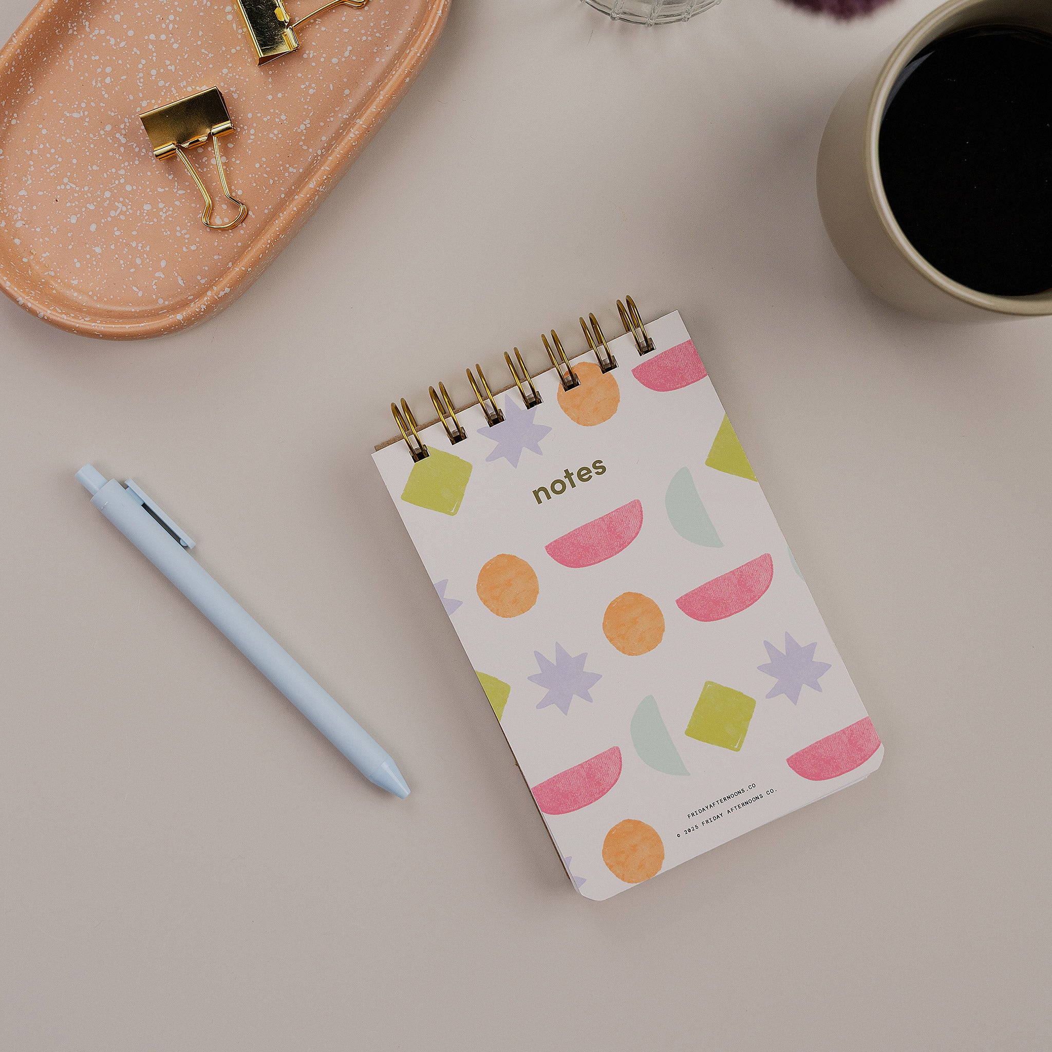 Mini Memo Notebook in Bright Shapes  cover by Friday Afternoons Co., shown on a desk with pen and accessories.