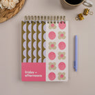 Lavender Scallop Workday Planner — top-spiral daily planner for work with pink and green patterned cover on desk.