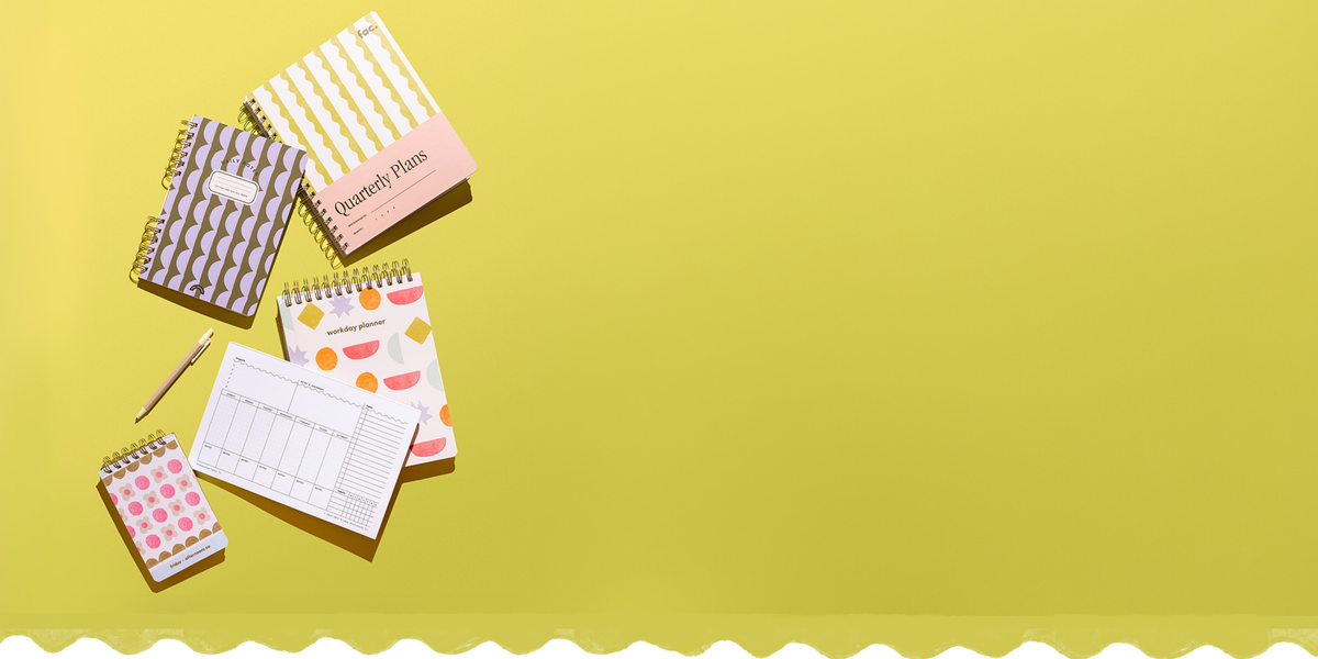 A set of colorful spiral-bound notebooks and a pen arranged on a bright yellow background, with a decorative scalloped white border along the bottom edge.