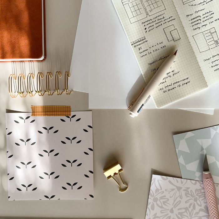 designer materials such as paper, clips, notebook gold spiral, sketchbook, and an assortment of materials for planner making