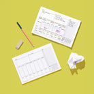 Weekly Task Tracker Notepad shown blank and filled out with pencil, eraser, and crumpled paper on a green background for weekly planning.