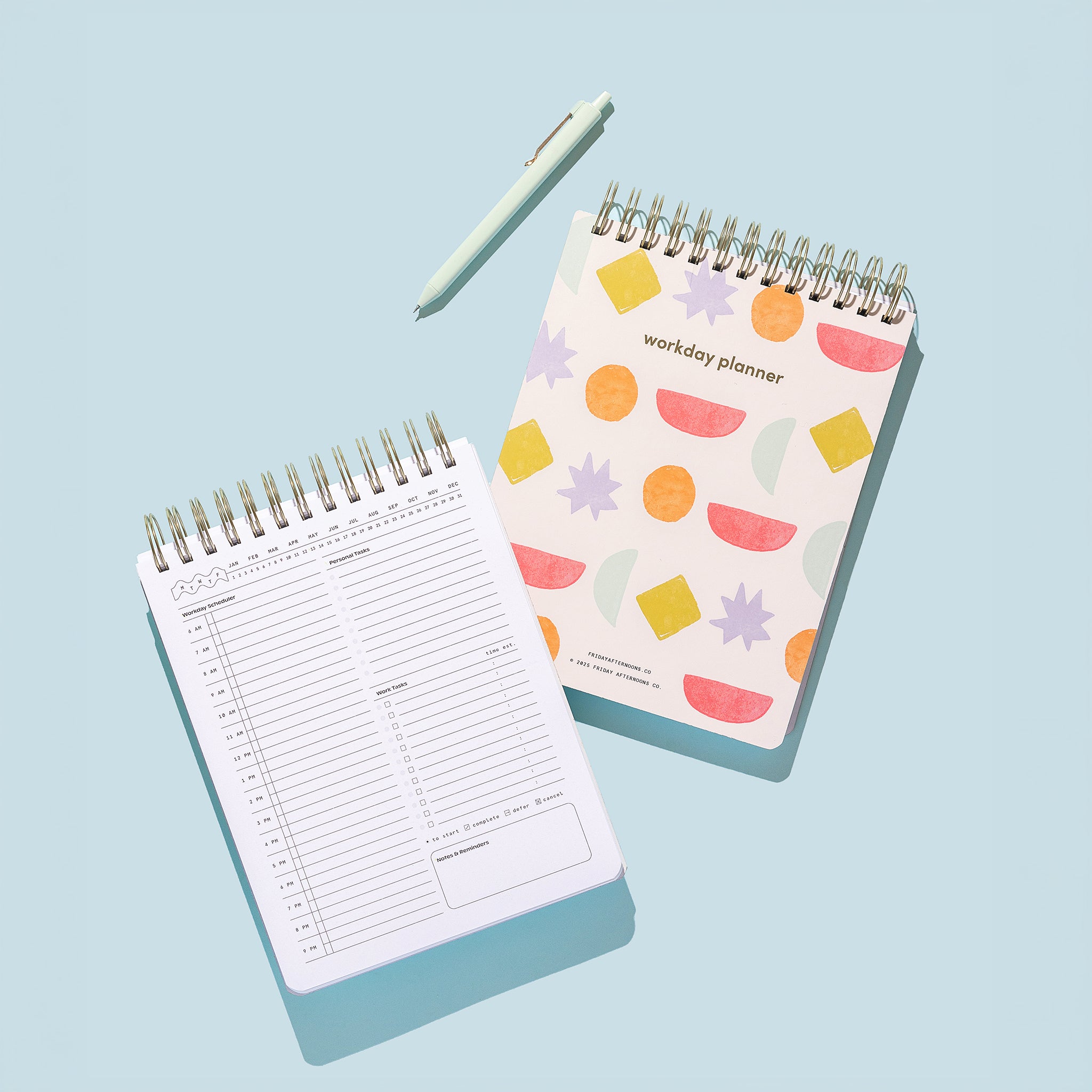 Bright Shapes Workday Planner with an open daily planning page, top-spiral binding, and pen on a light blue background.